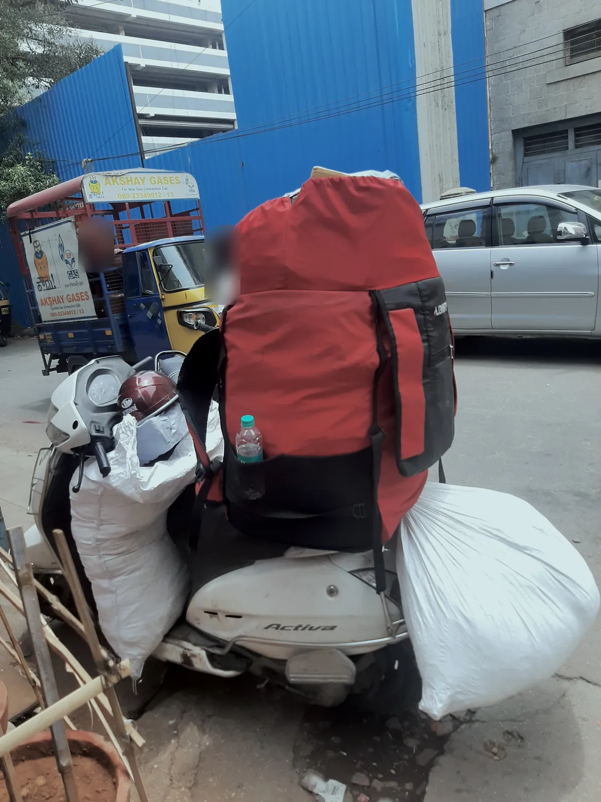 A parked scooter with a big red bag on the seat and white sacks tied to both sides