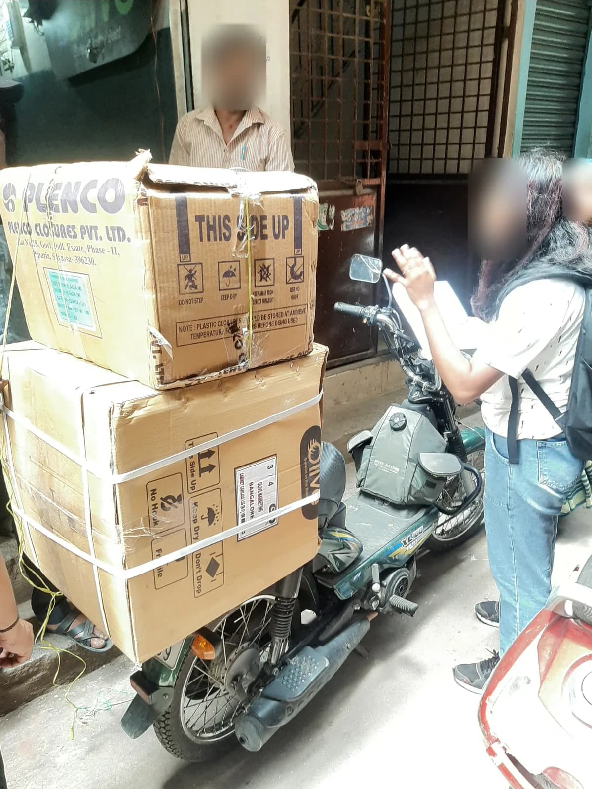 Two large cardboard cartons tied to a scooter outside a shop while our team talks to the shopkeeper
