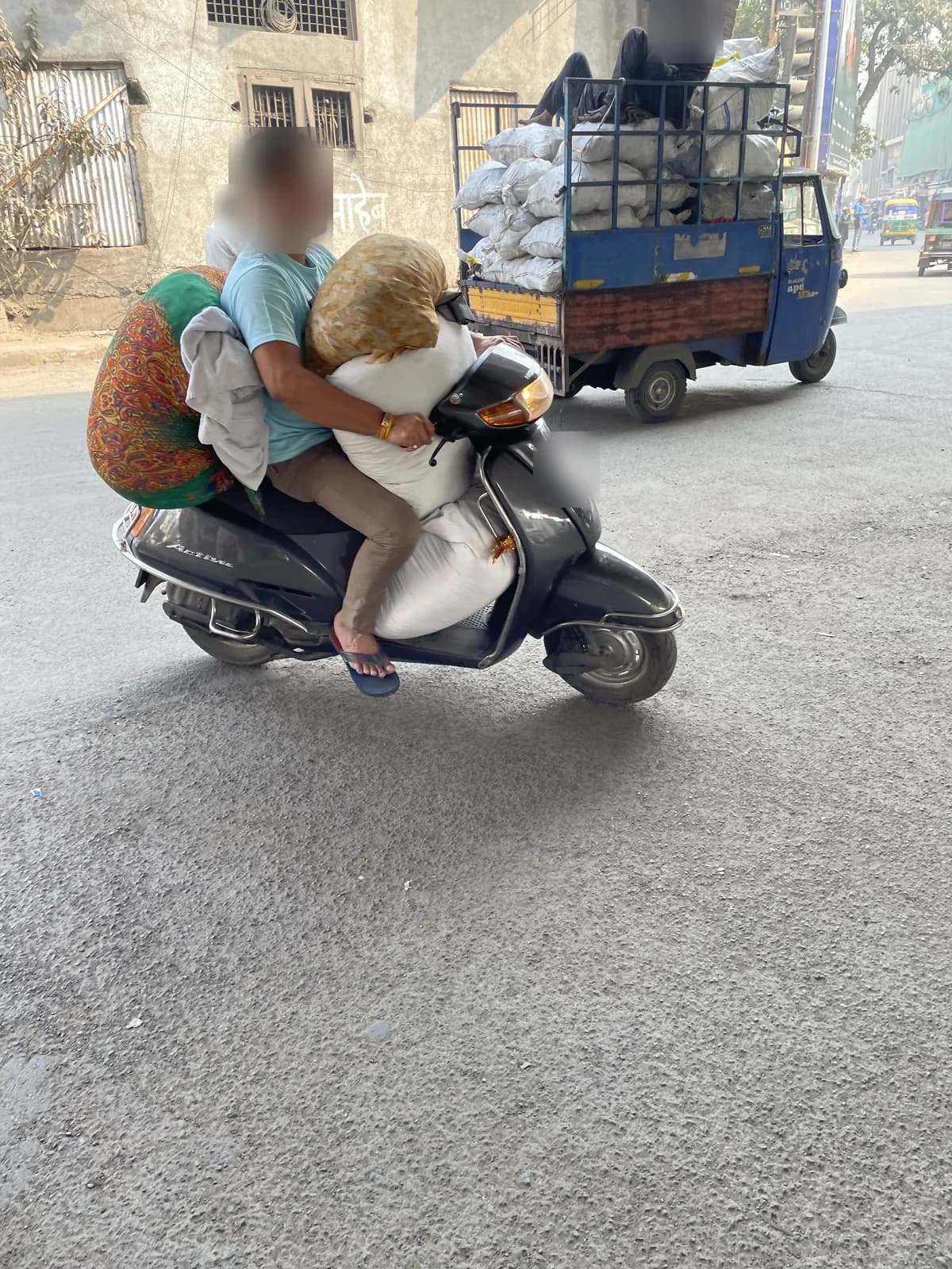 A man riding a scooter with a woman behind him and a large white bale wedged between them