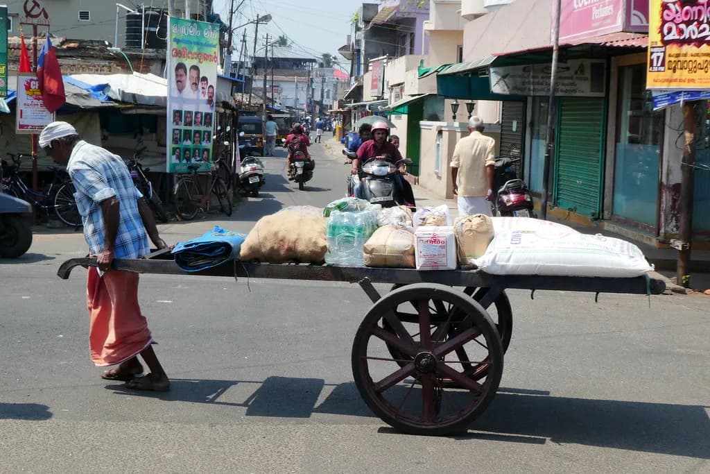 A man pulling a long wooden handcart loaded with sacks down a street in Fort Kochi