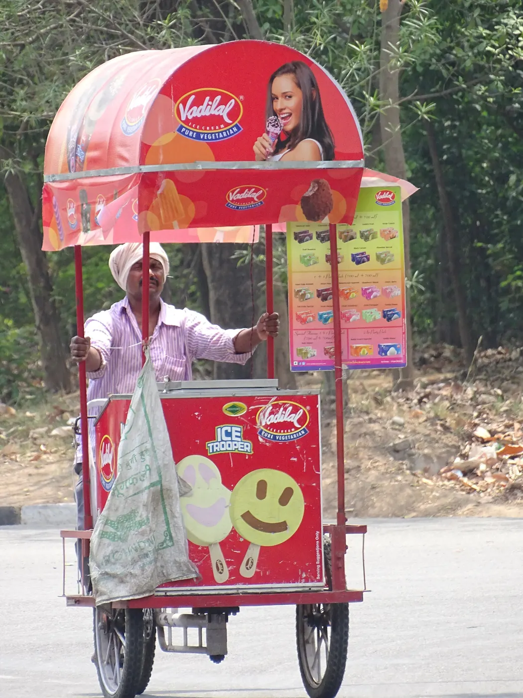 An ice-cream seller standing behind a red branded cart under a canopy
