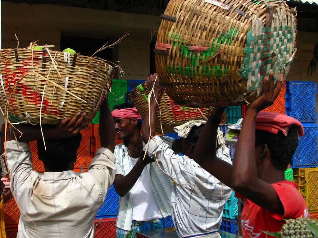 Porters carrying large woven baskets of produce on their heads at Koyambedu market in Chennai