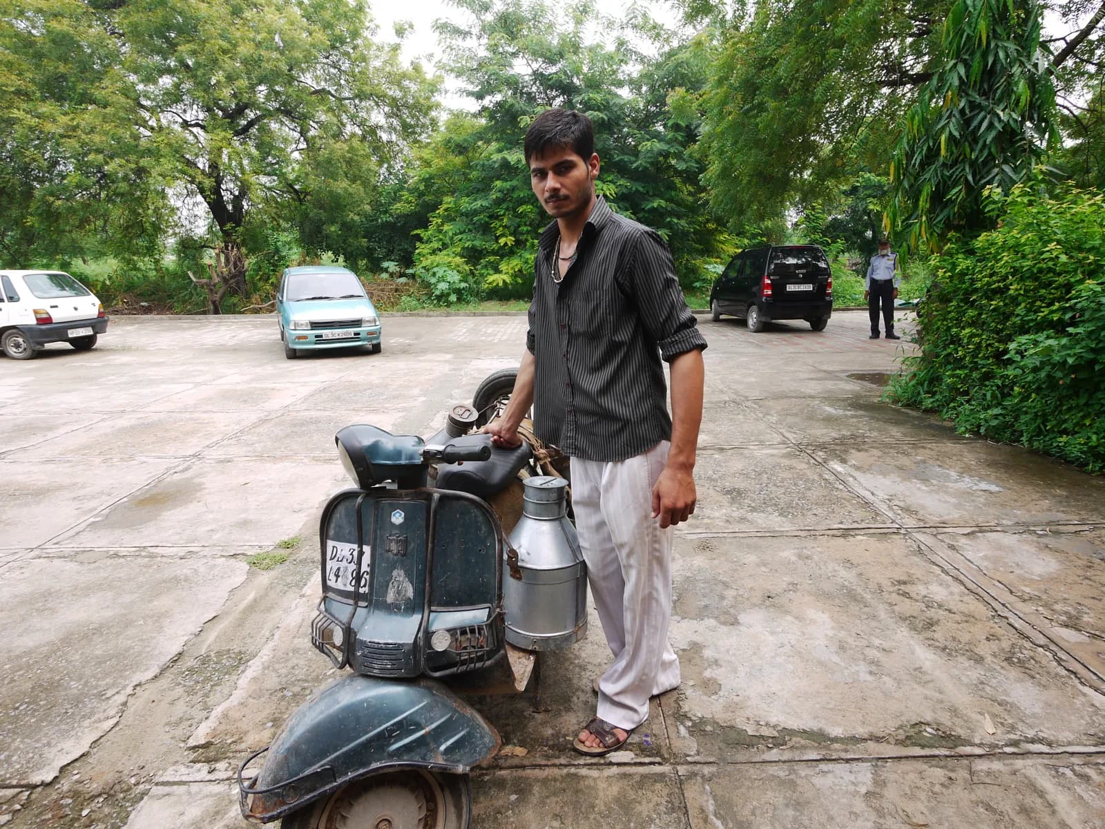 A milkman standing beside his scooter with steel milk cans tied on both sides