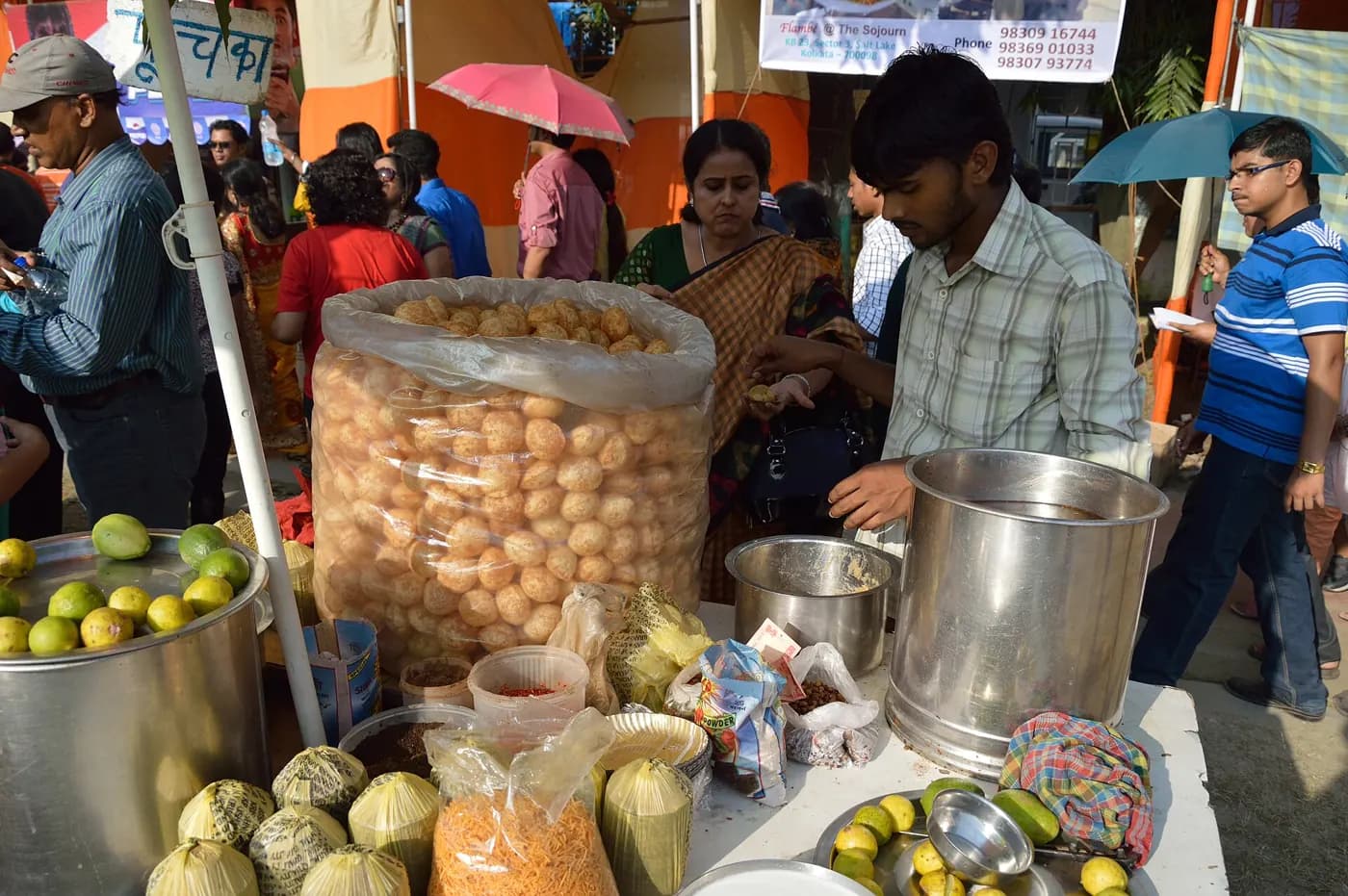 A pani-puri stall with a large jar of puris, steel pots and fresh produce, the seller serving customers