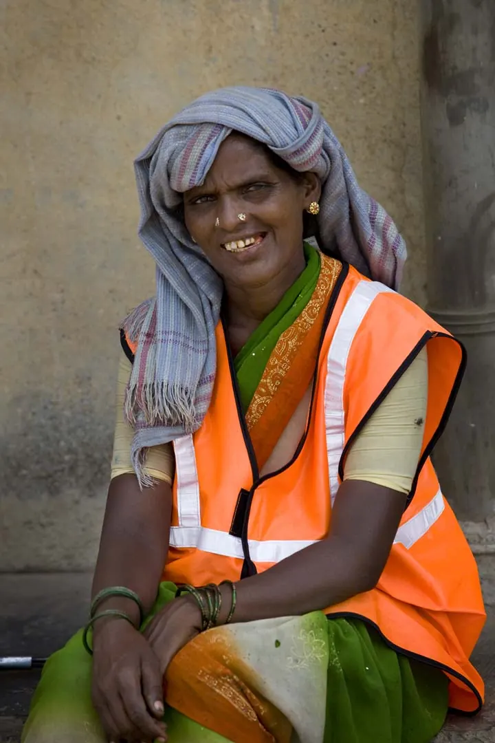 A street cleaner in an orange high-visibility vest, seated and smiling